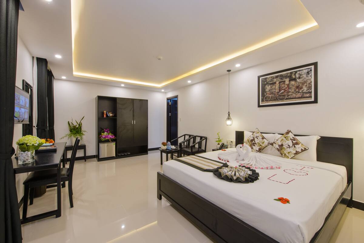 A modern hotel room with a large bed, a desk, and a dining area.