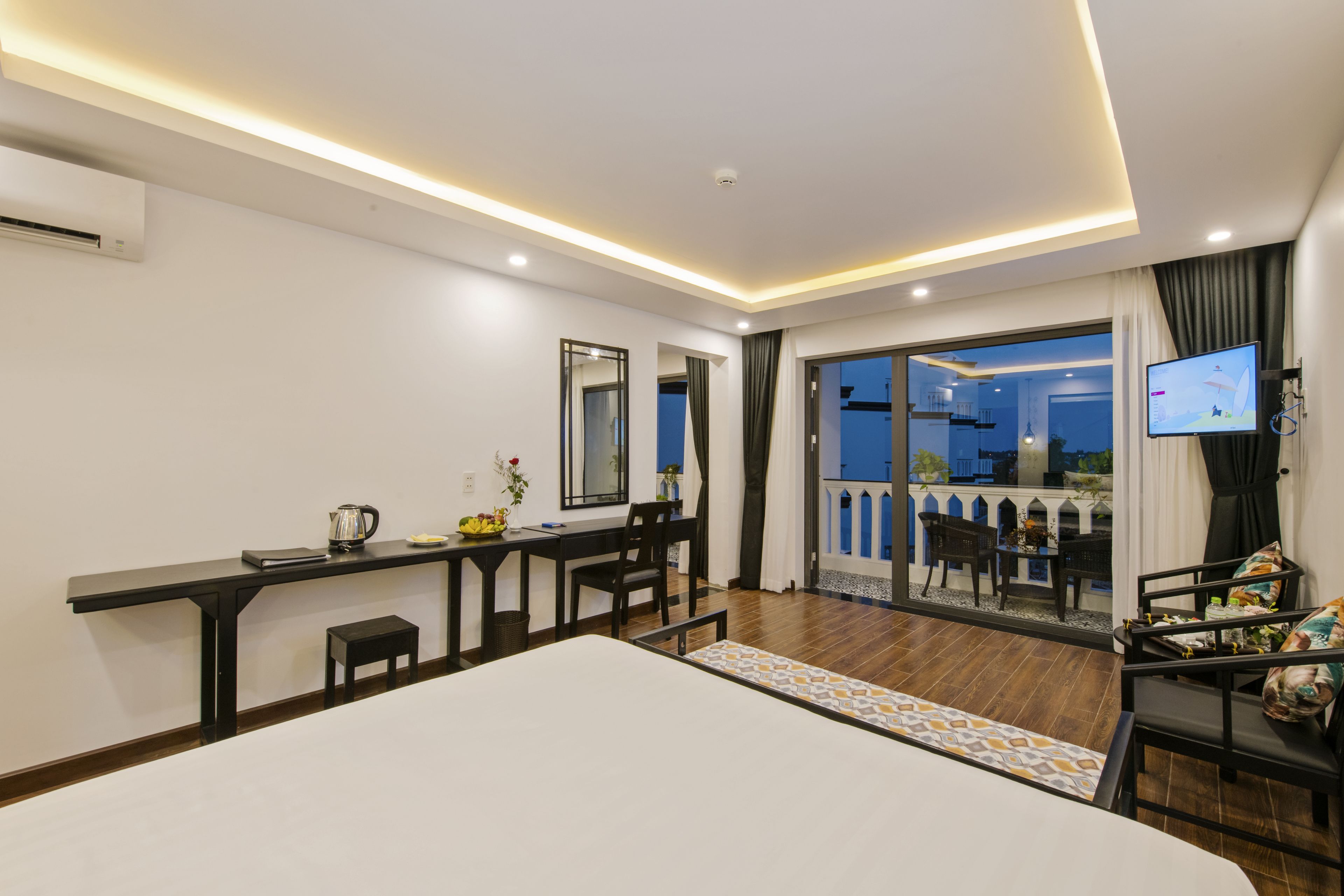 A modern hotel room with a balcony, a dining area, and a TV.