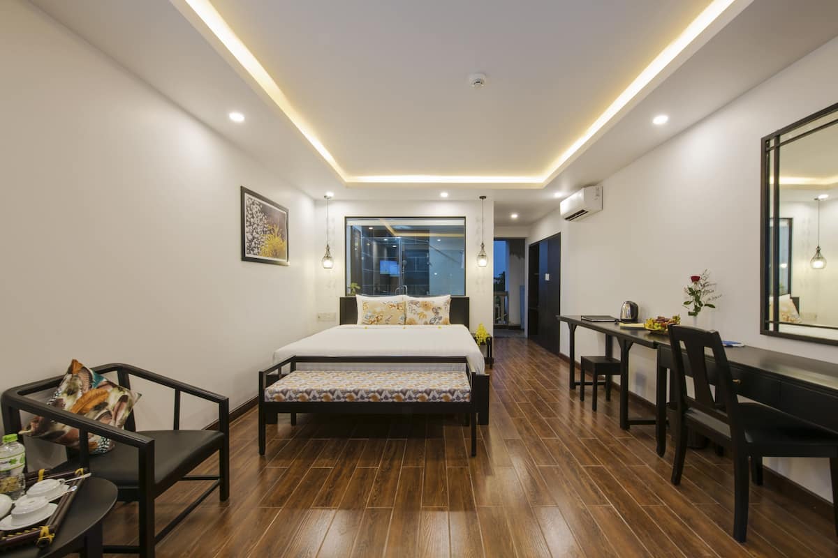 A modern hotel room with a large bed, a dining table, and a seating area.