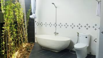 A bathroom with a freestanding bathtub, a toilet, and a bamboo plant.