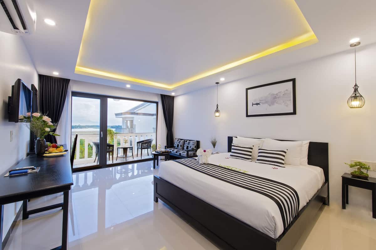 A modern hotel room with a large bed, a desk, a balcony with a view, and a ceiling with recessed lighting.