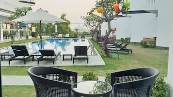 A pool area with lounge chairs and umbrellas, surrounded by greenery and a white building.