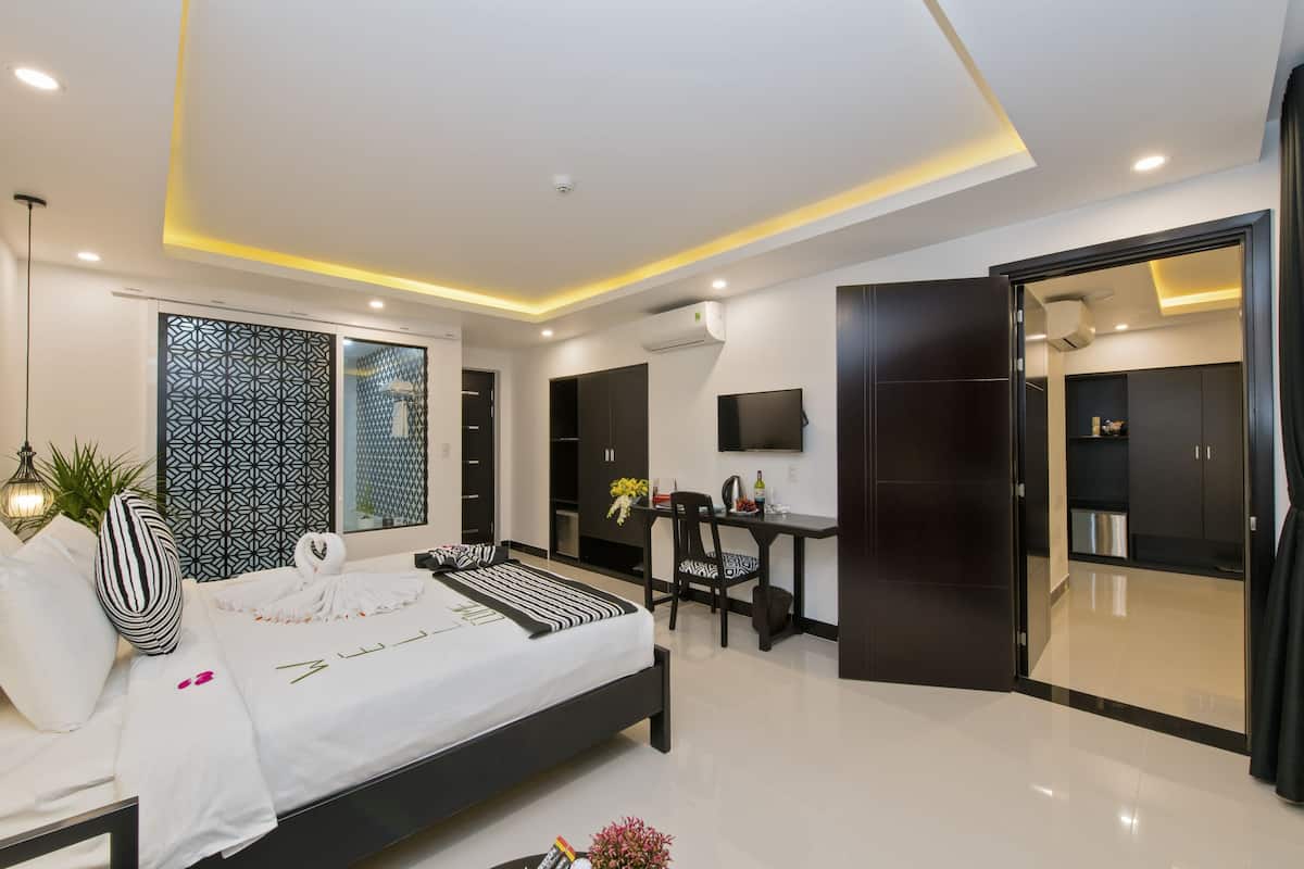 A modern hotel room with a bed, desk, and wardrobe.