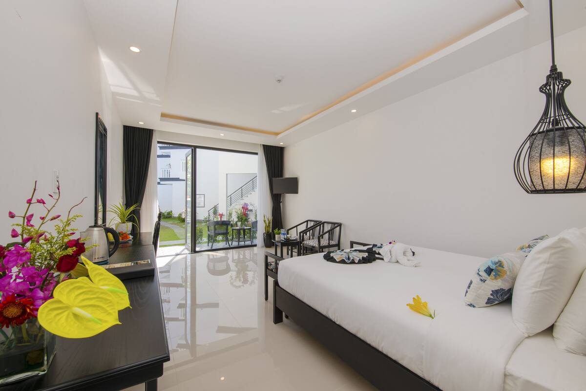 A modern hotel room with a large bed, a desk with a computer, a chair, and a view of the outdoors.