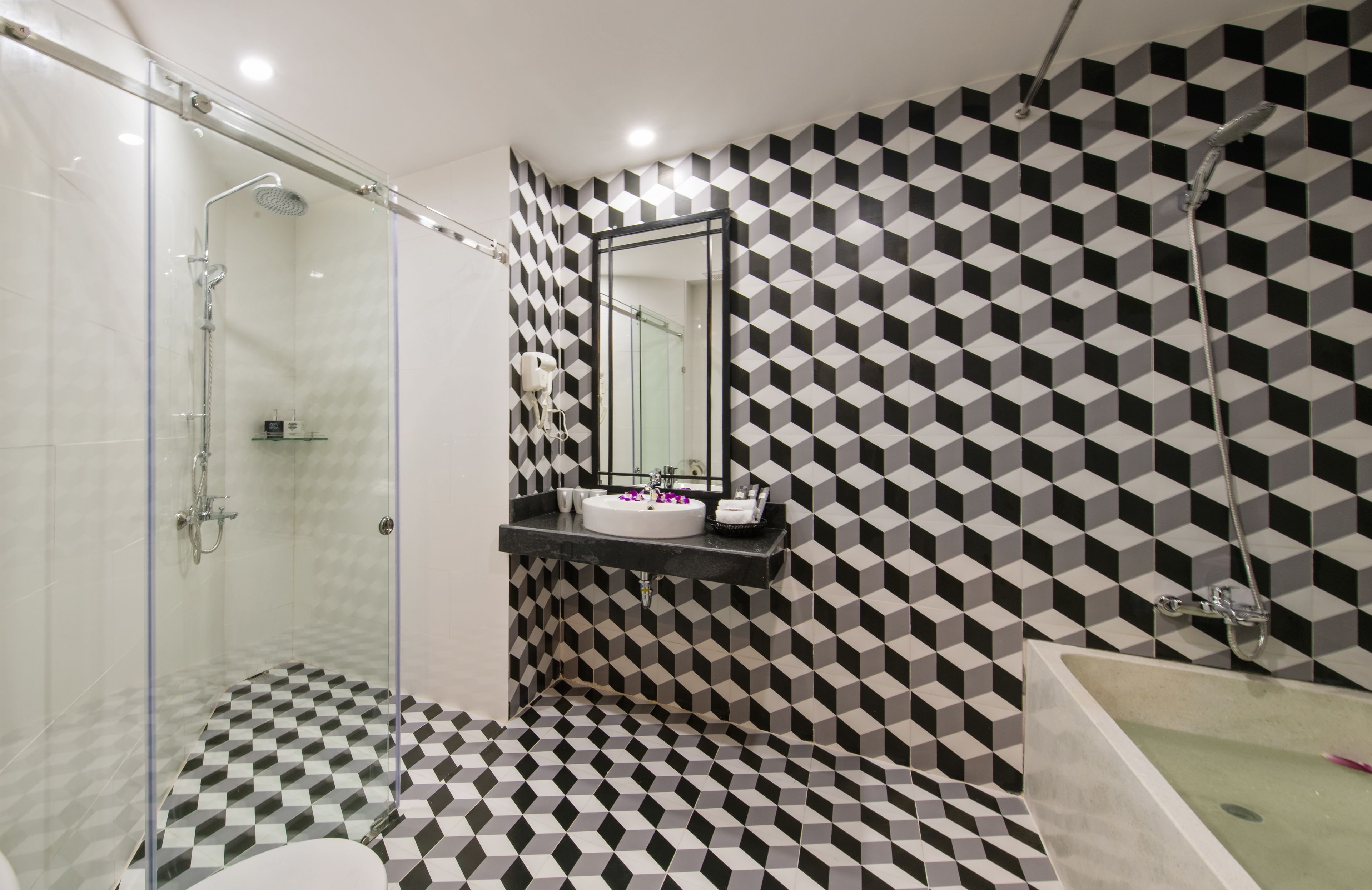 Un baño moderno con un pared de diseño geométrico, cabina de ducha de vidrio, lavabo con espejo y bañera.