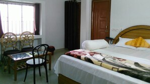 A bedroom with a bed, a wooden headboard, a window with curtains, a table with chairs, and an air conditioning unit.