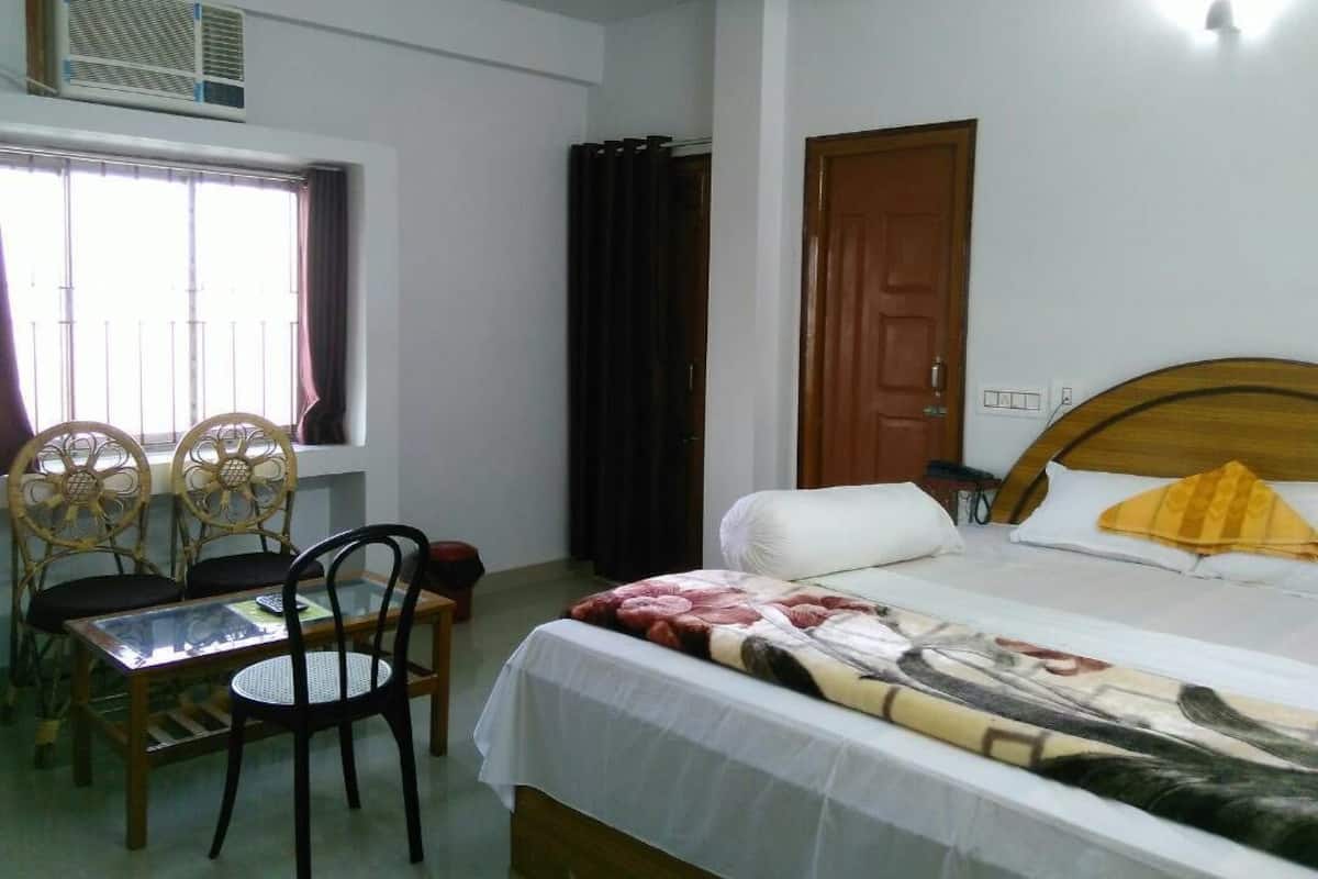 Une chambre à coucher comprenant un lit, une tête de lit en bois, une fenêtre avec des rideaux, une table avec des chaises et un appareil de climatisation.