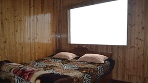 A wooden room with a bed, a window, and a wooden floor.