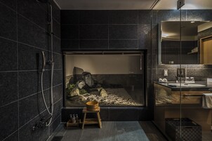 A modern bathroom with a large glass shower enclosure, a wooden stool, and a sink with a mirror.