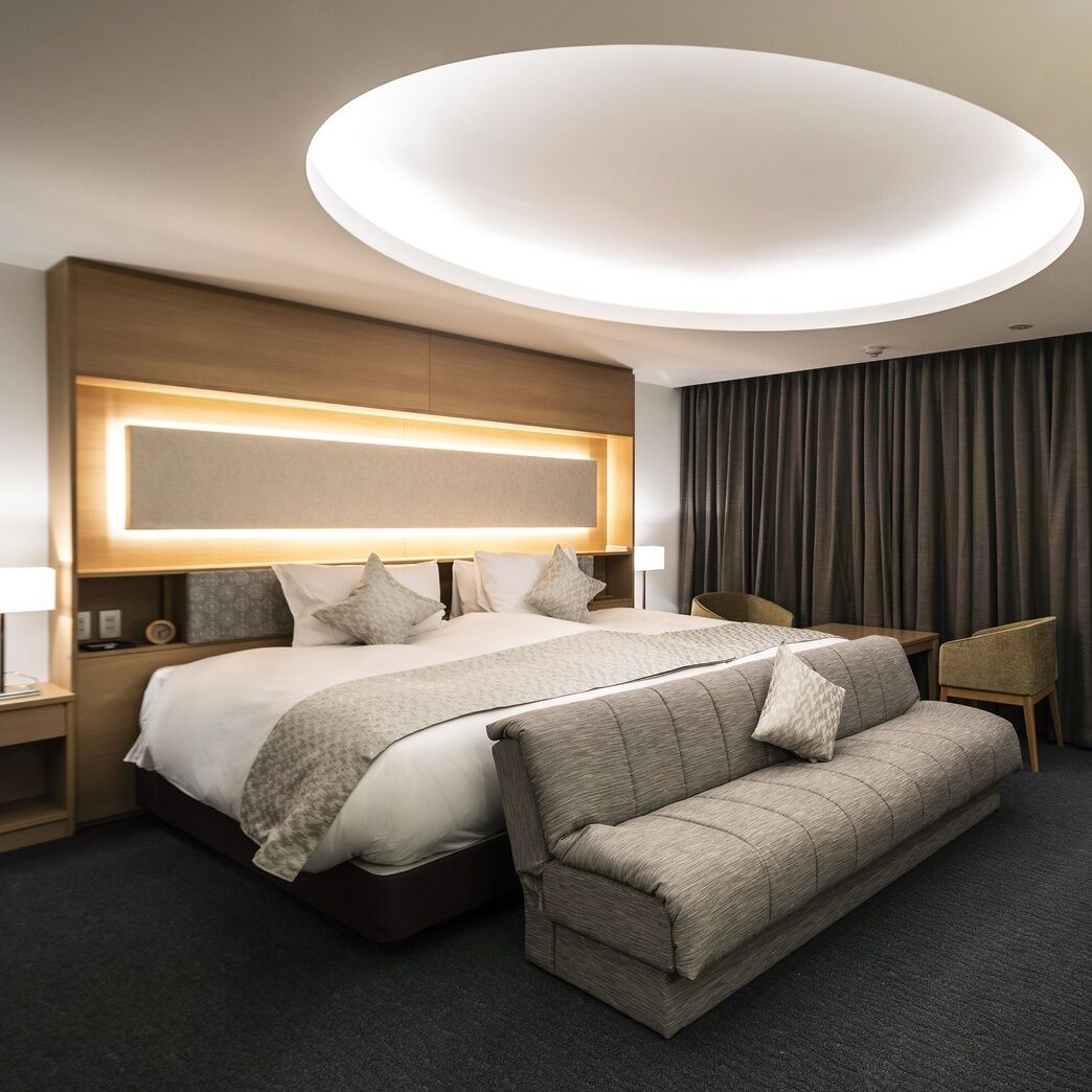 A modern hotel room with a large bed, a sofa, a desk, and a ceiling light fixture.