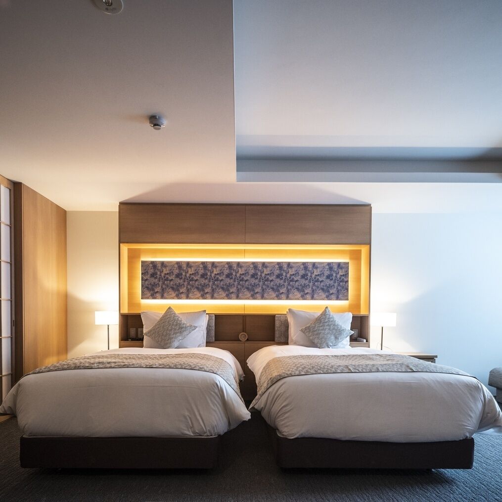 A hotel room with two beds, a large wall-mounted artwork, and a ceiling light fixture.