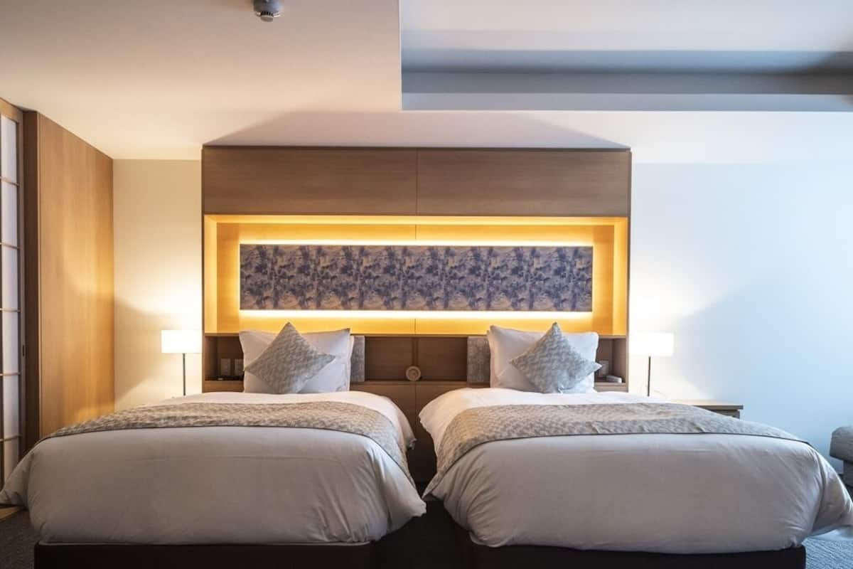 Quarto de hotel com duas camas, uma obra de arte grande na parede e um lustre.