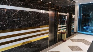 Un ascensor moderno con detalles metálicos, una pared de mármol con franjas doradas y blancas, y un piso limpio y pulido.