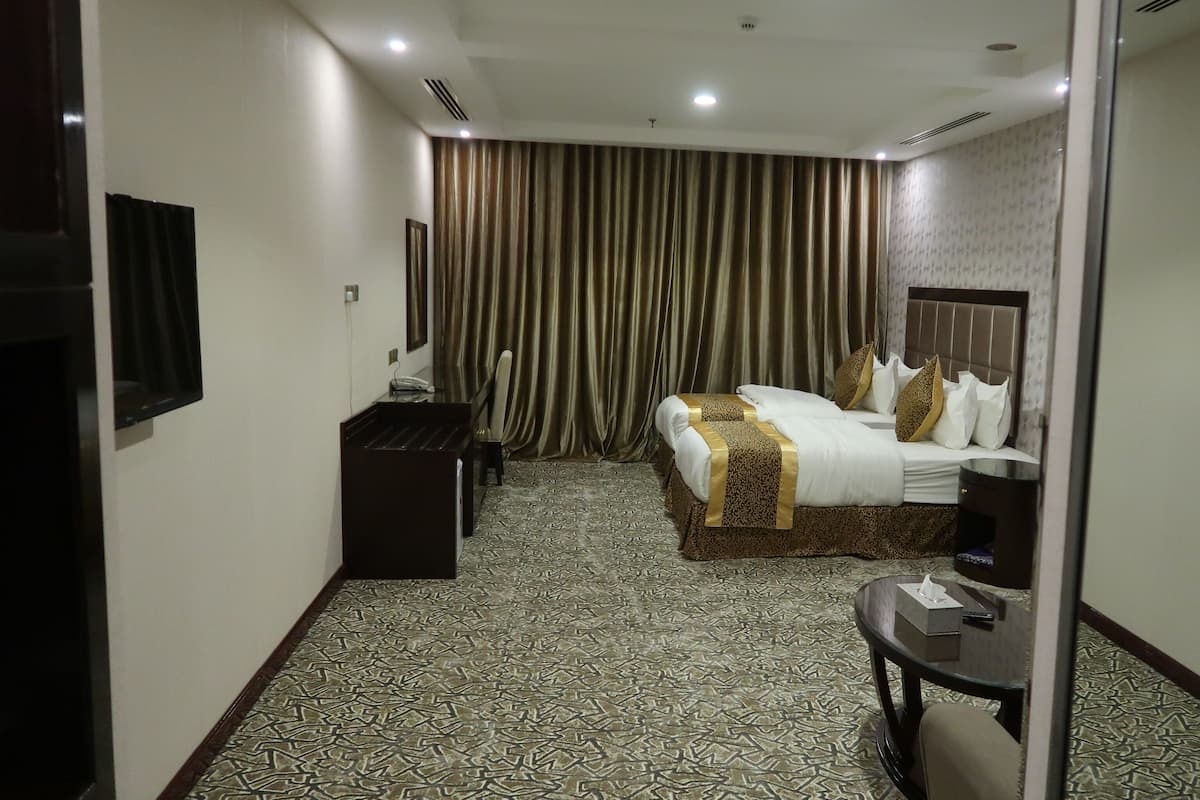 A hotel room with a large bed, a desk, a chair, a TV, and a curtain.