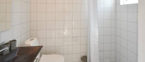 Une petite salle de bain avec des carreaux blancs, des toilettes, un lavabo et un rideau de douche.
