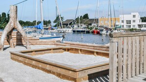 Eine Holzstele mit einer Betonplattform, umgeben von einem Holzzaun, und ein Yachthafen mit Booten im Hintergrund.