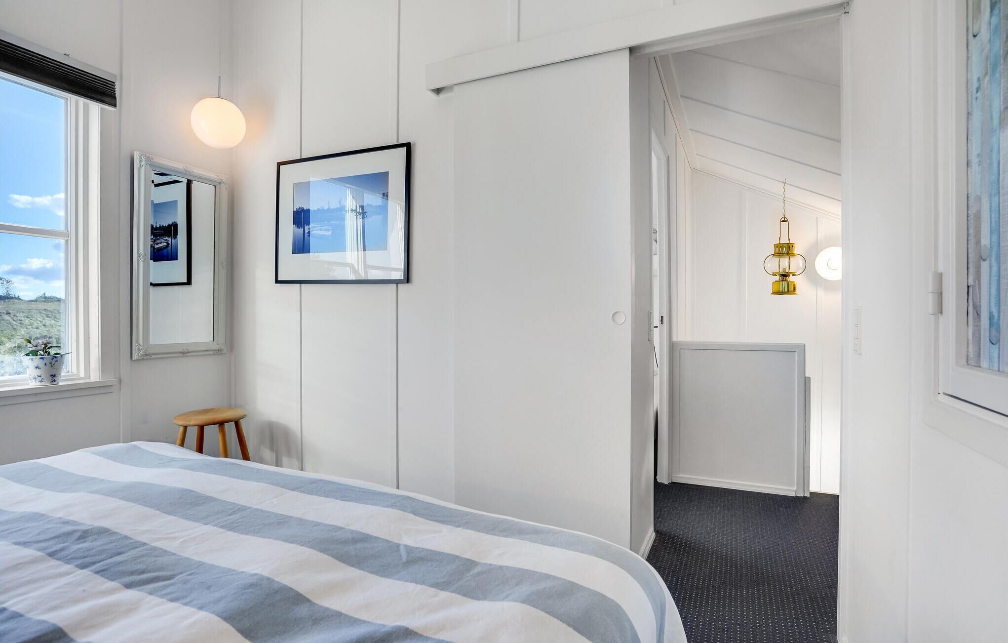 A bedroom with a bed, a window, a door, and a hallway leading to another room.