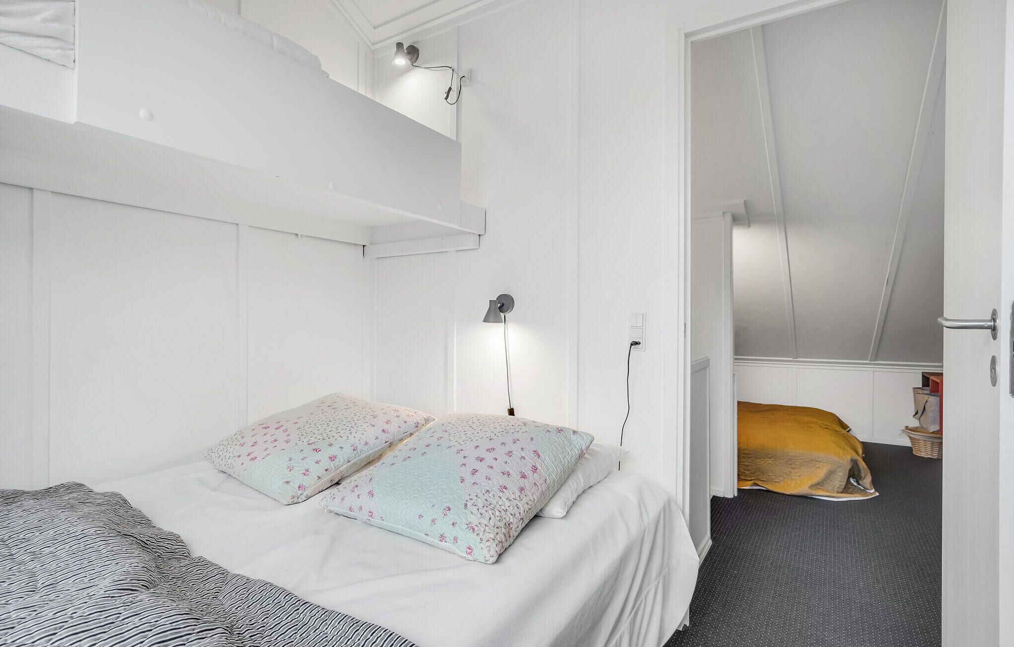 Una camera da letto compatta, arredata in bianco, con un letto a castello, una lampada da comodino e un piccolo armadio.