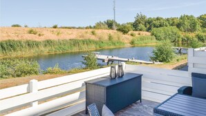 Eine Terrasse mit Korbmöbeln mit Blick auf einen ruhigen Fluss, umgeben von viel Grün und einem weißen Zaun.