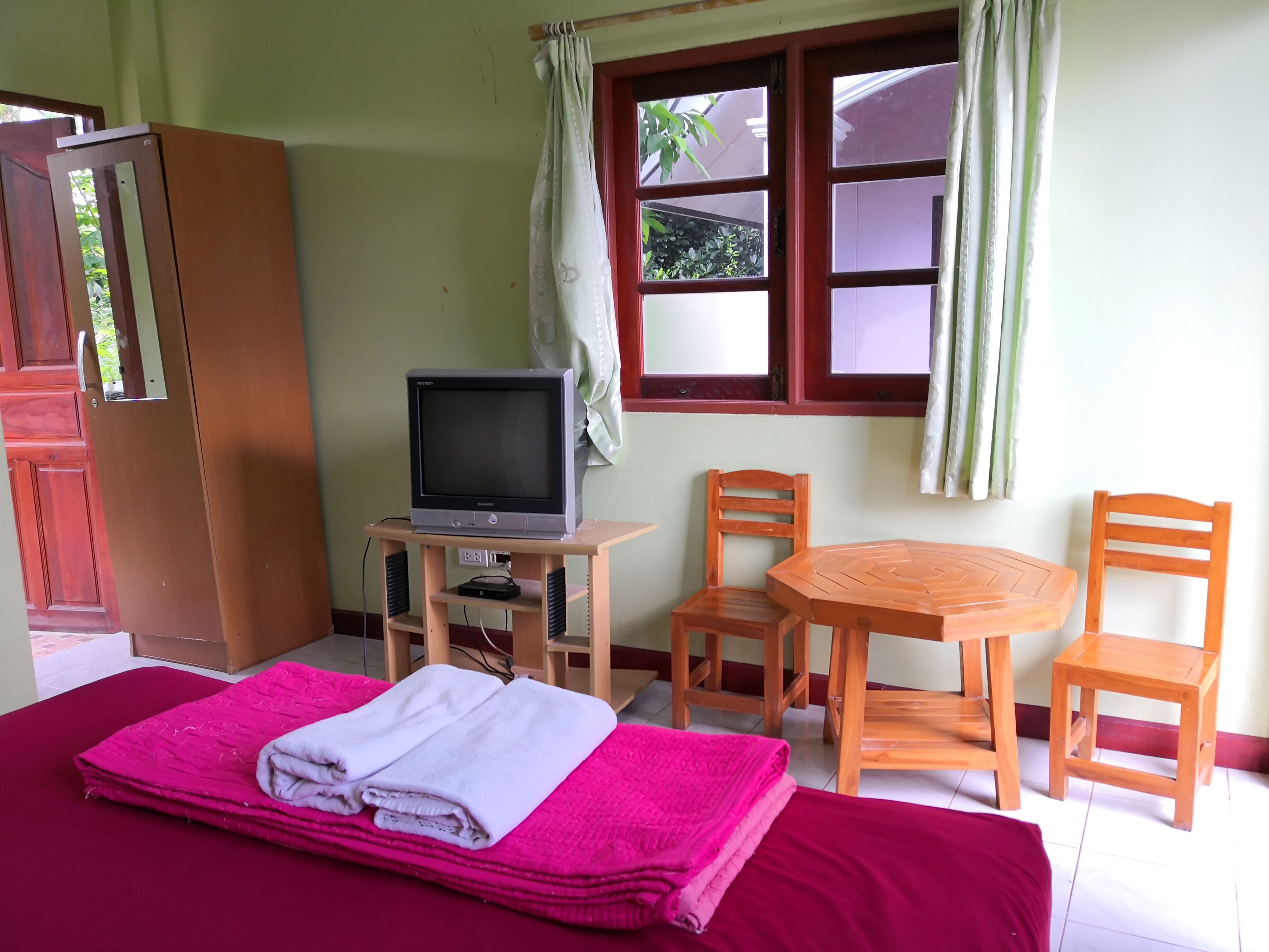 A room with a bed, a television on a stand, a small table, two chairs, and a wardrobe.