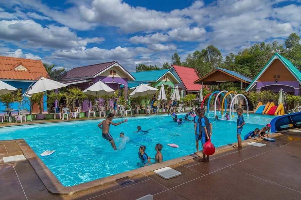 Uma área de piscina com edifícios coloridos, guarda-sóis e espreguiçadeiras.