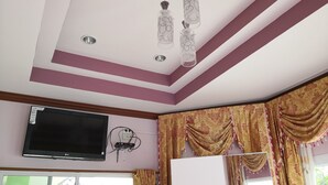 Une pièce dotée d’un téléviseur à écran plat fixé au mur, d’un luminaire au plafond et d’une fenêtre avec des rideaux.
