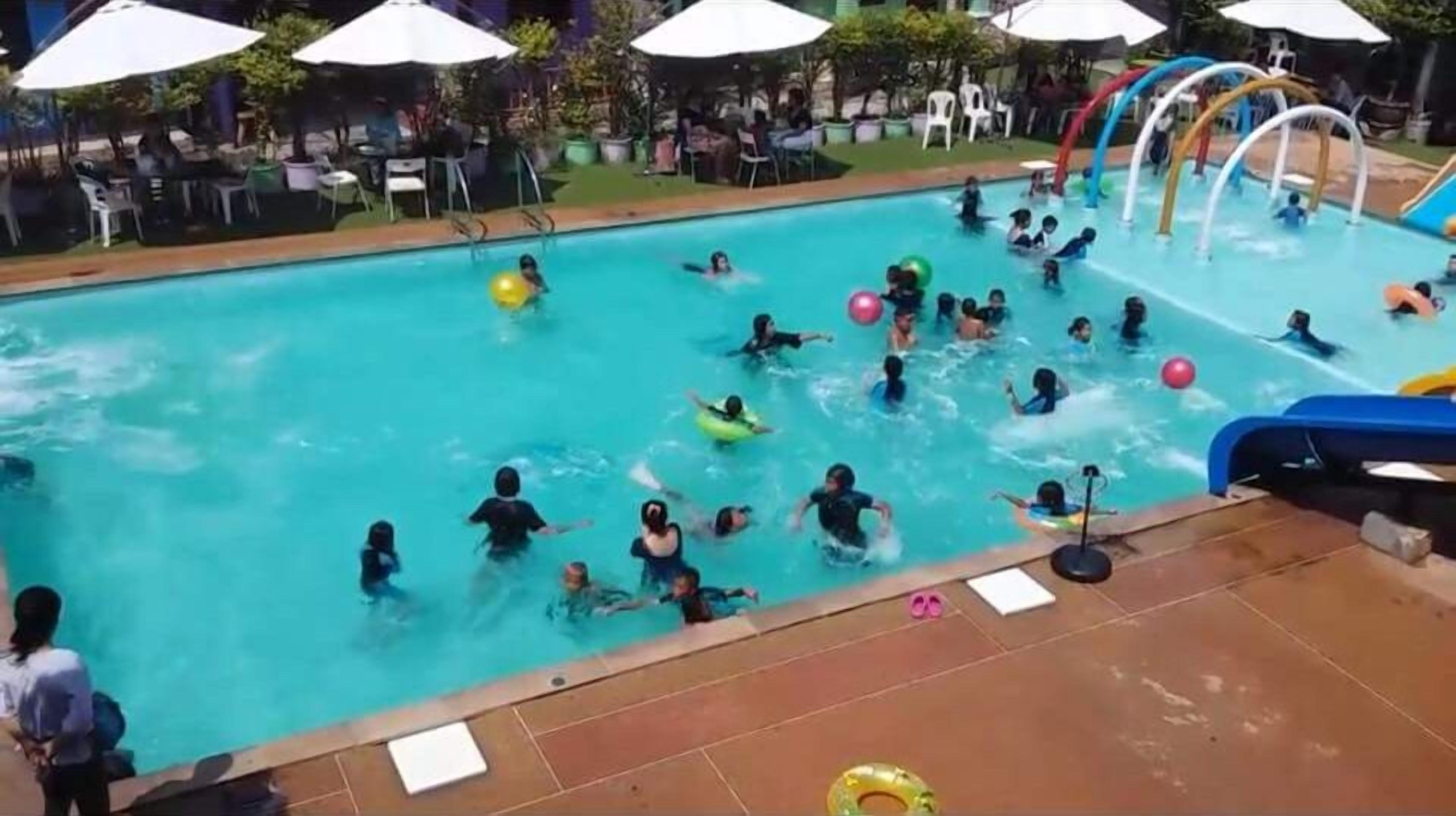 A swimming pool with multiple lanes, surrounded by umbrellas and chairs, indicating a poolside area.