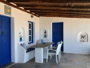 A covered outdoor dining area with a stone floor, white walls, and blue doors. - Villa Elena (Mykonos)