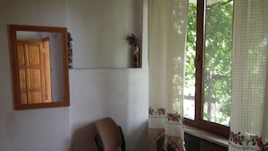 Una habitación con una silla de madera, una mesita y una ventana con cortinas florales.