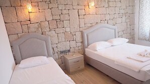 Un dormitorio con dos camas, una pared de piedra y una mesita de noche con lámpara.