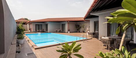Una piscina con borde de baldosas, rodeada de plantas en macetas y mobiliario de exterior.