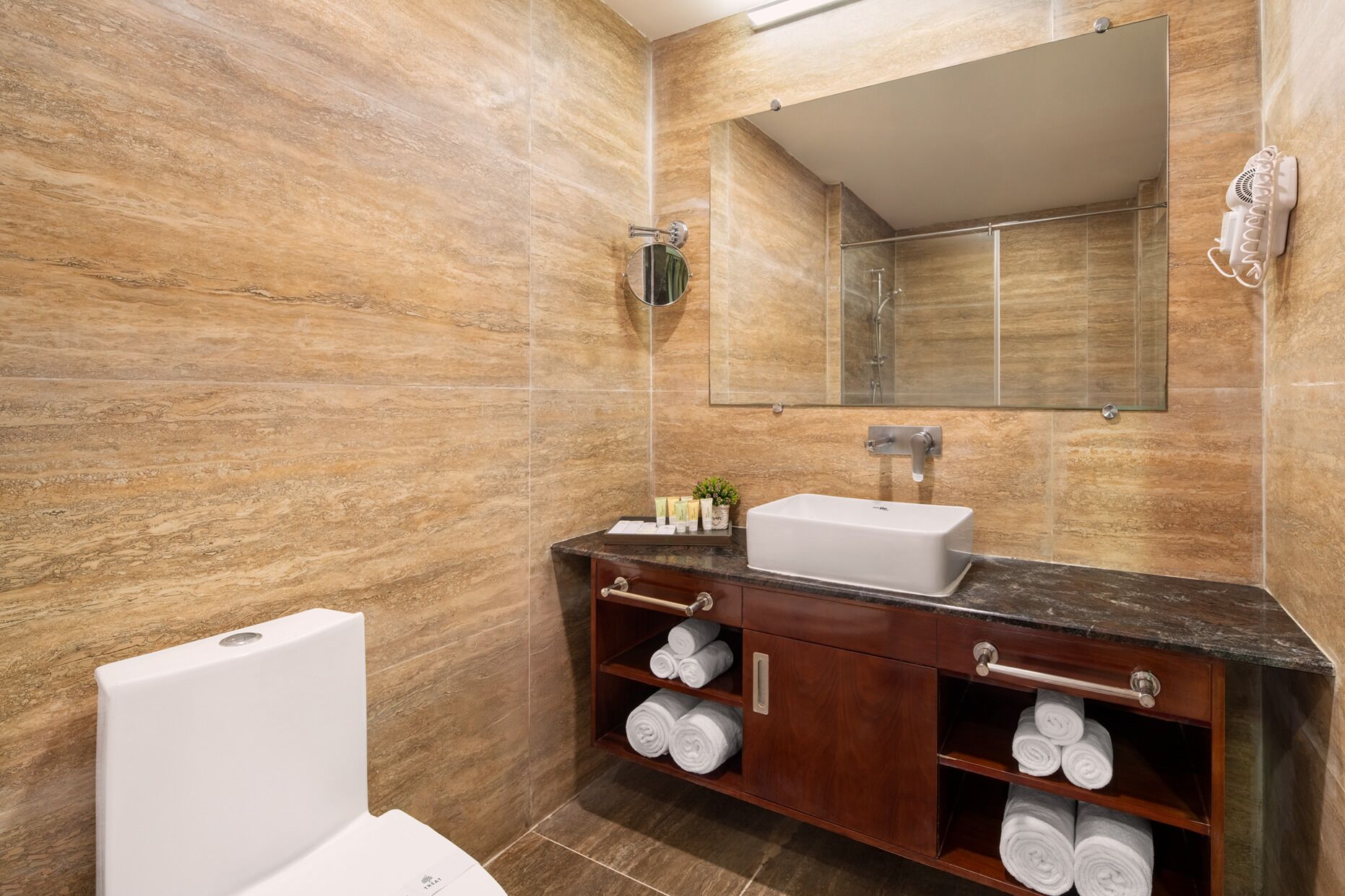 A bathroom with a marble wall, a sink, a mirror, a towel rack, and a toilet.