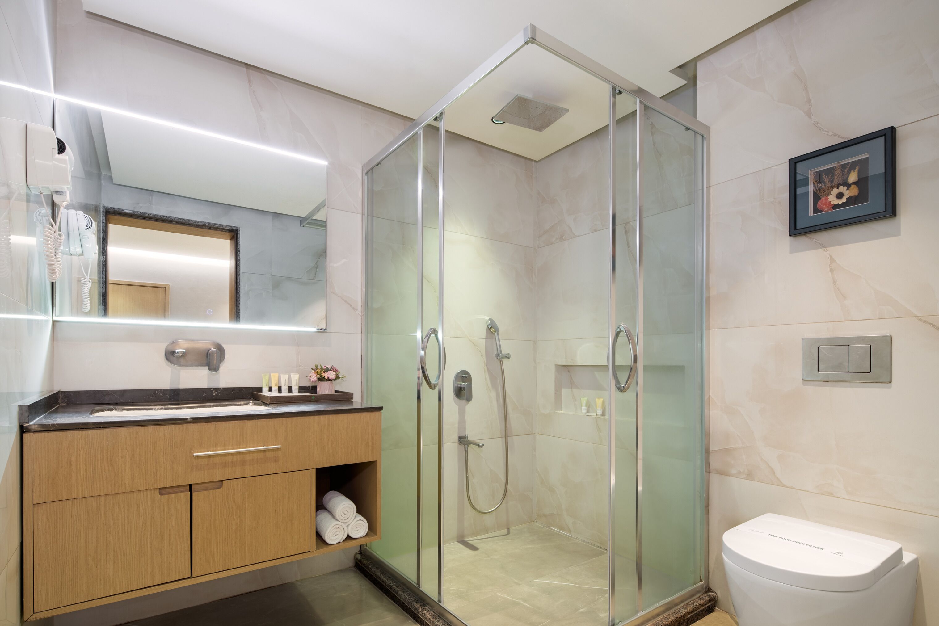 Et moderne badeværelse med en glasafskærmet brusebad, et træbord med spejl og et toilet.