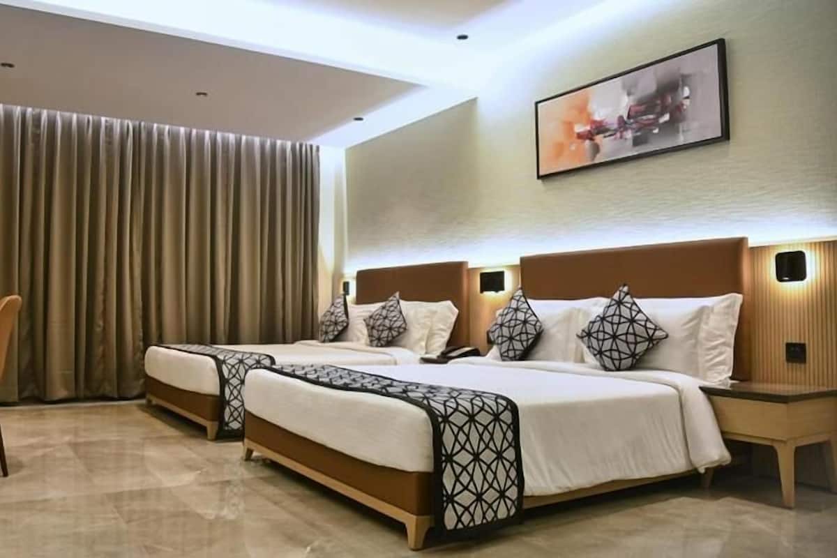 Habitación de hotel con dos camas, un escritorio, una silla y un ventanal con cortinas.