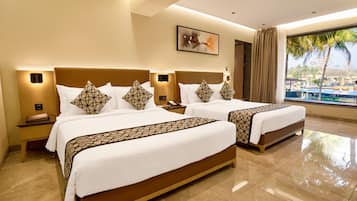 Two double beds with geometric-patterned bedspreads and matching pillows, a nightstand, and a table with a view of palm trees and a pool.