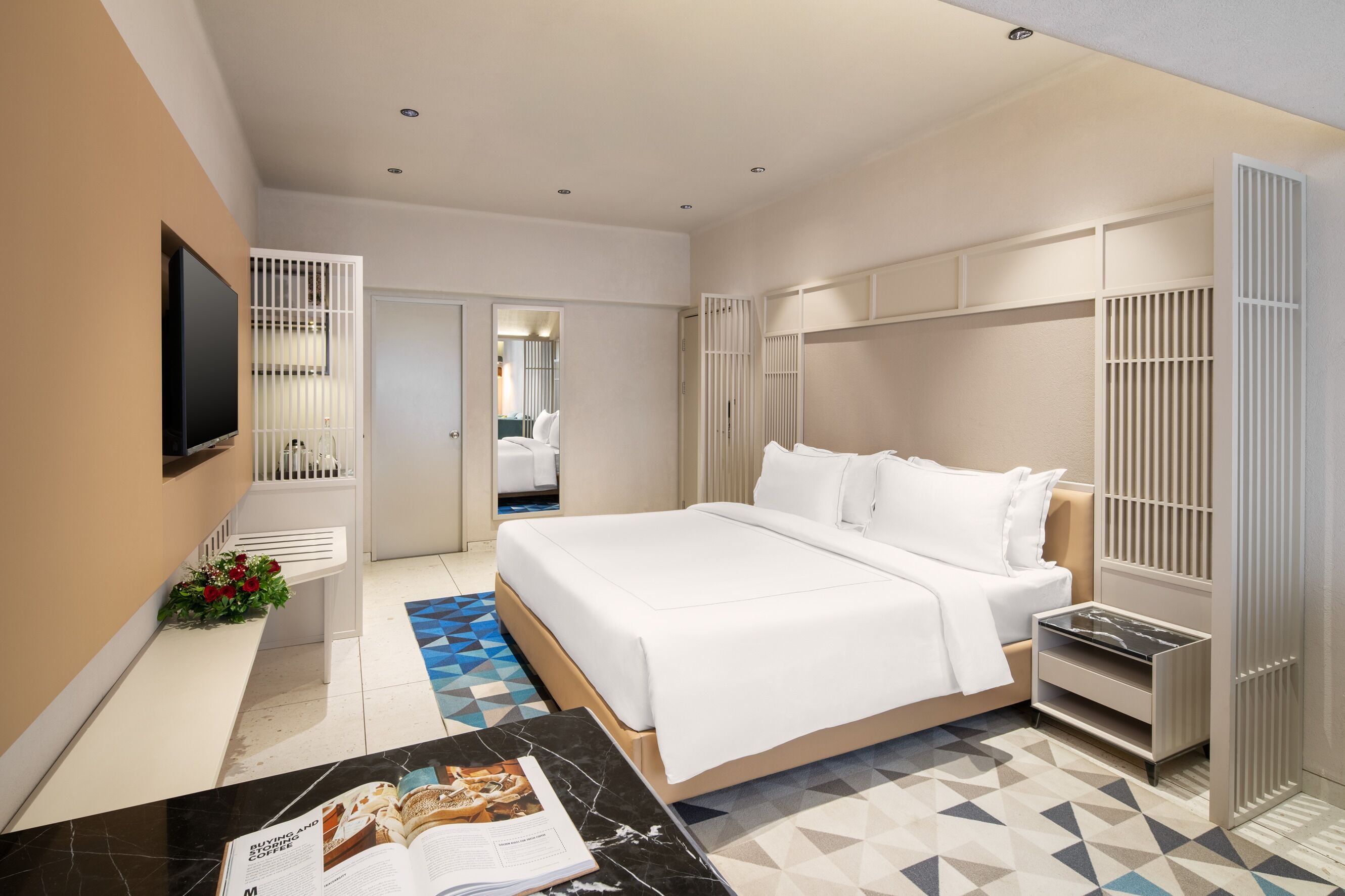 Habitació d'hotel moderna amb un llit gran, una televisió, un escriptori amb una revista i un armari.