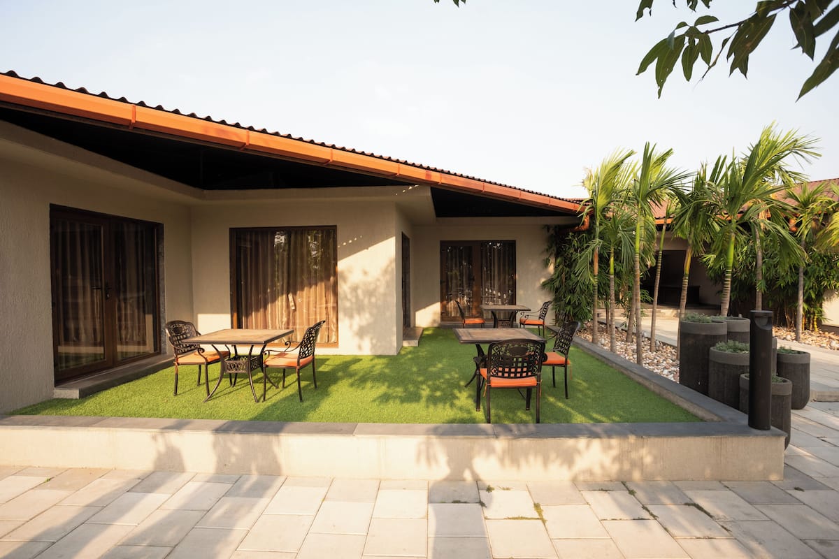 Un patio con zona de comedor, mobiliario exterior y un pequeño jardín con palmeras.