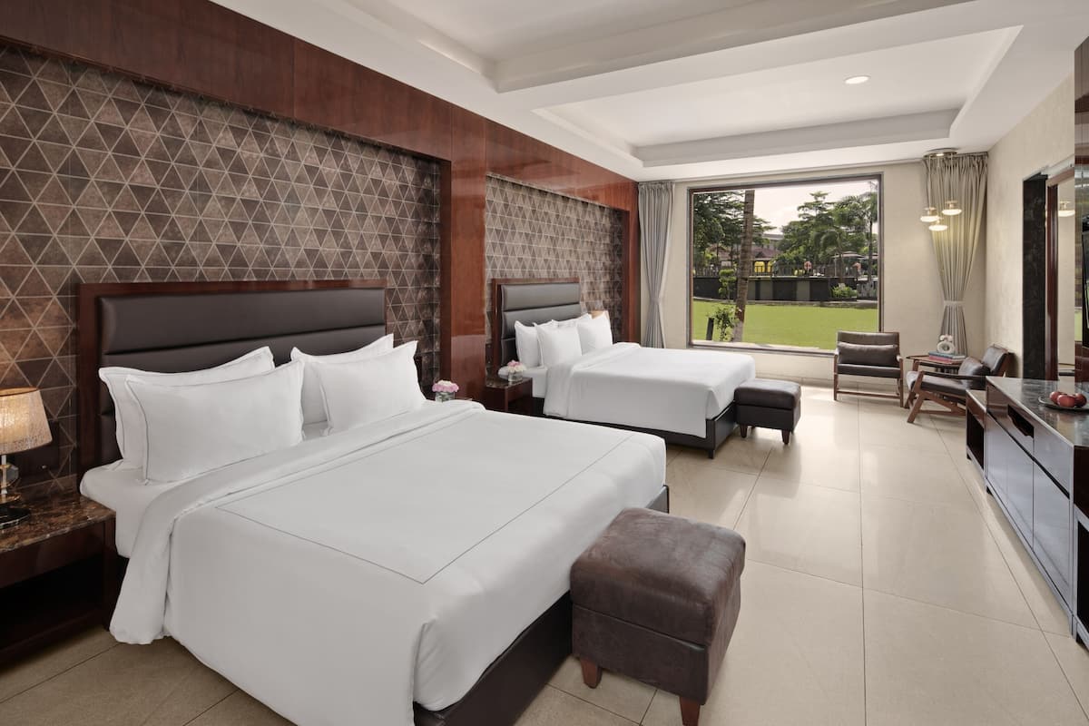 Habitación de hotel con dos camas, un escritorio, una silla y vistas a un jardín.