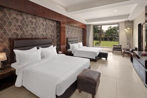 Habitación de hotel con dos camas, un escritorio, una silla y vistas a un jardín.