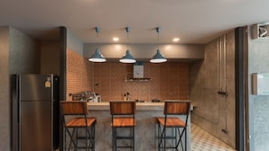 A kitchen with a brick backsplash, a stainless steel refrigerator, and three bar stools. - Bed & Bike Hostel (Chiang Rai)