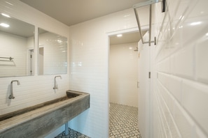 Un baño con paredes de azulejos blancos, un tocador de madera y un suelo estampado.