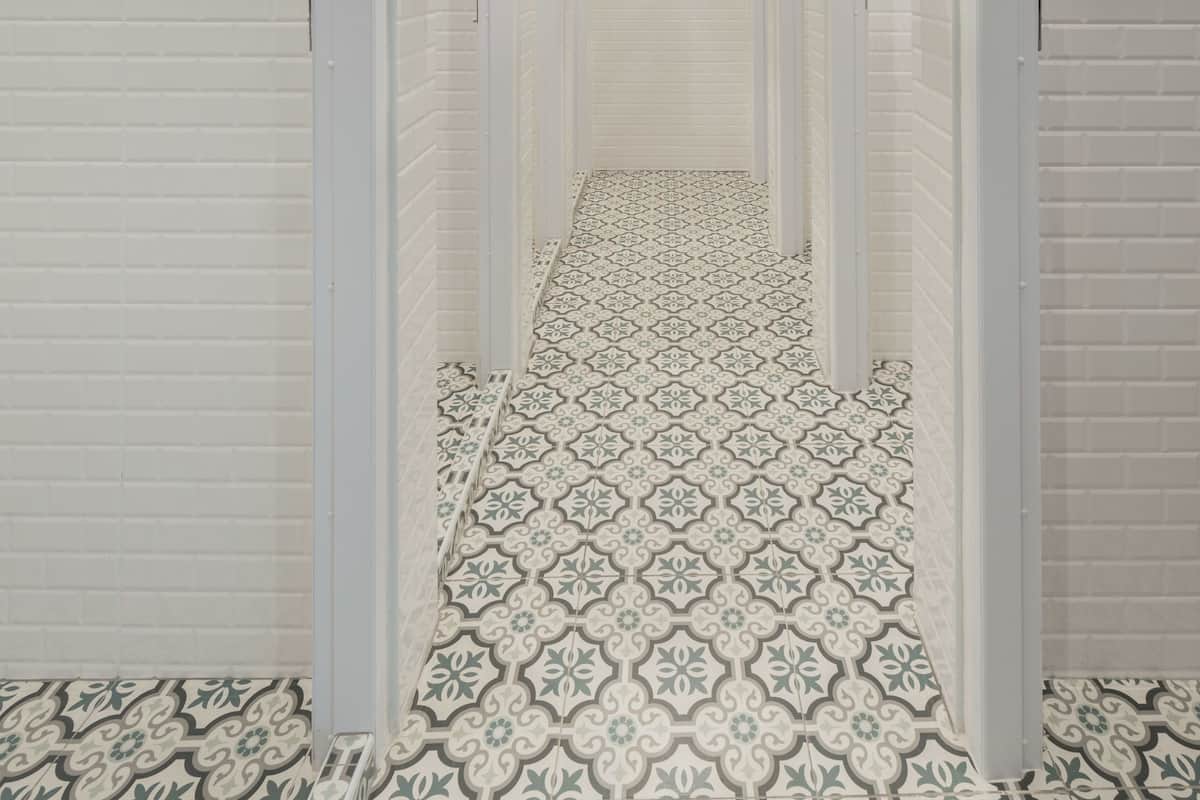 Corredor com paredes de azulejos brancos e ladrilhos estampados no chão.