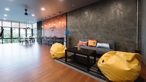 A modern interior with a brick wall, a sofa with pillows, a coffee table, and yellow bean bags. - Bed & Bike Hostel (Chiang Rai)