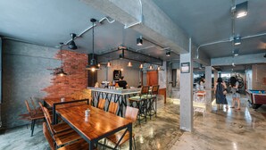 A spacious cafe with exposed brick walls, wooden tables, and hanging pendant lights. - Bed & Bike Hostel (Chiang Rai)