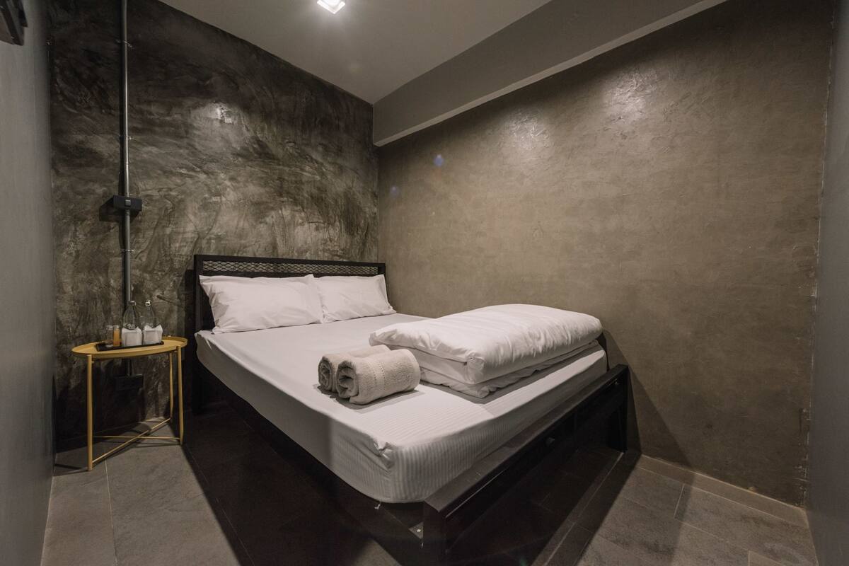 Quarto moderno com uma cama grande, mesa de cabeceira com produtos de higiene e parede texturizada.