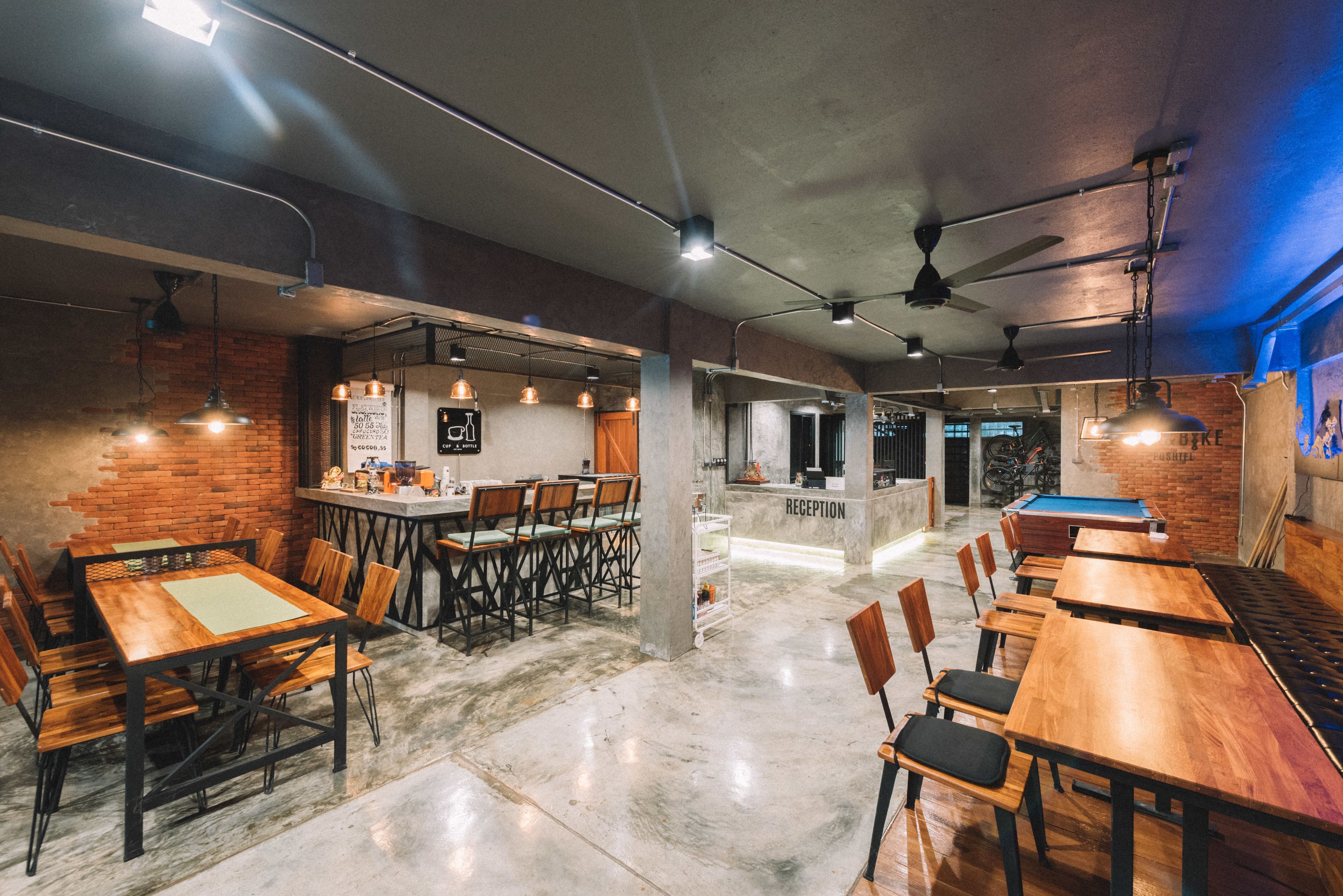 Un grand espace intérieur aménagé avec plusieurs tables et chaises en bois, un comptoir d’accueil et une table de billard.