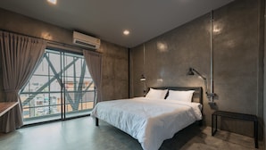 A modern bedroom with a large bed, a view of a cityscape through a large window, and an air conditioning unit on the wall. - Bed & Bike Hostel (Chiang Rai)