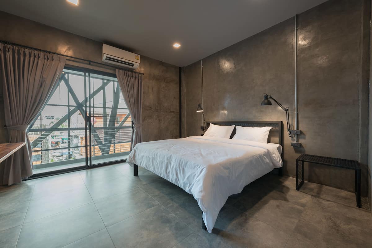 Quarto moderno com uma cama grande, vista para a cidade através de uma janela ampla e um ar condicionado na parede.