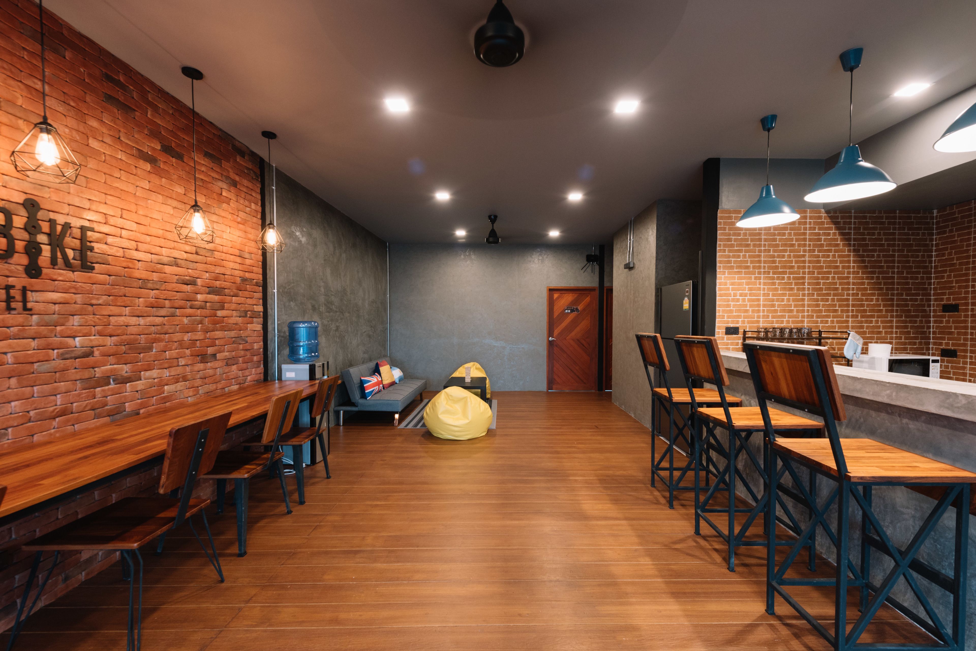 Un café moderno con mesas y sillas de madera, una pared de ladrillo e iluminación colgante.