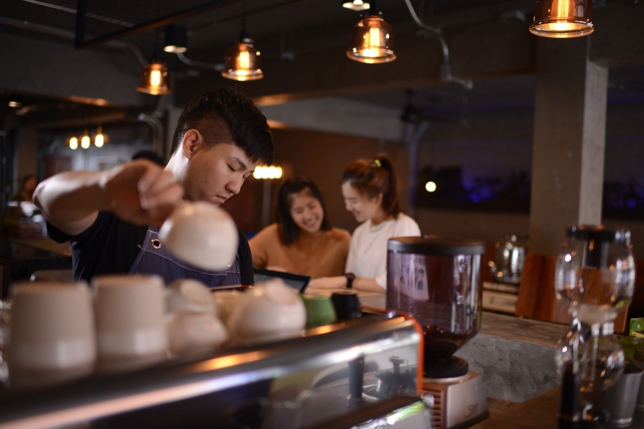 A barista preparing coffee in a modern cafe with industrial lighting and a rustic ambiance.